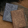 A brown leopard print passport holder with personalized name embossing resting on a wooden surface.
