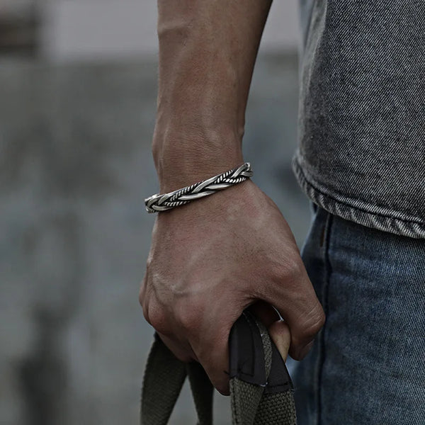 Gros plan d'une main portant un bracelet à torsade en argent sterling sur un fond gris flou.