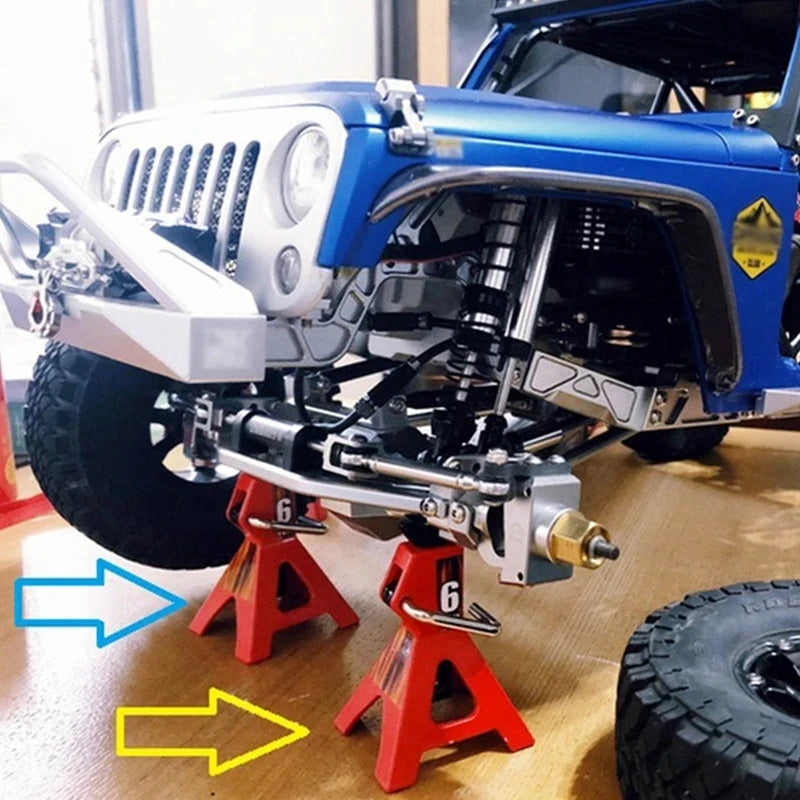 A blue motorcycle is supported by red metal jack stands on a wooden floor.