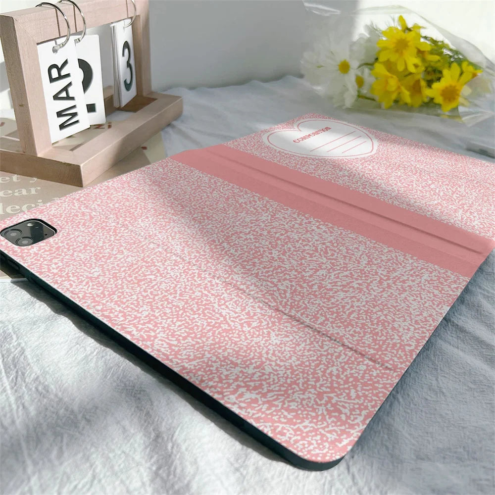Pink composition notebook iPad case with a pencil holder lying on a white sheet.