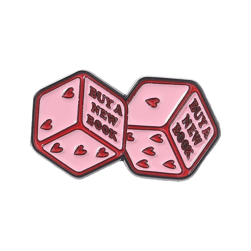 A set of pink enamel pins shaped like dice, featuring a book theme and heart accents.