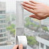 A hand is shown applying self-adhesive fiberglass screen repair tape to a window or screen surface.