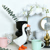 A white resin goose key holder sculpture next to a potted orchid and green eucalyptus leaves.