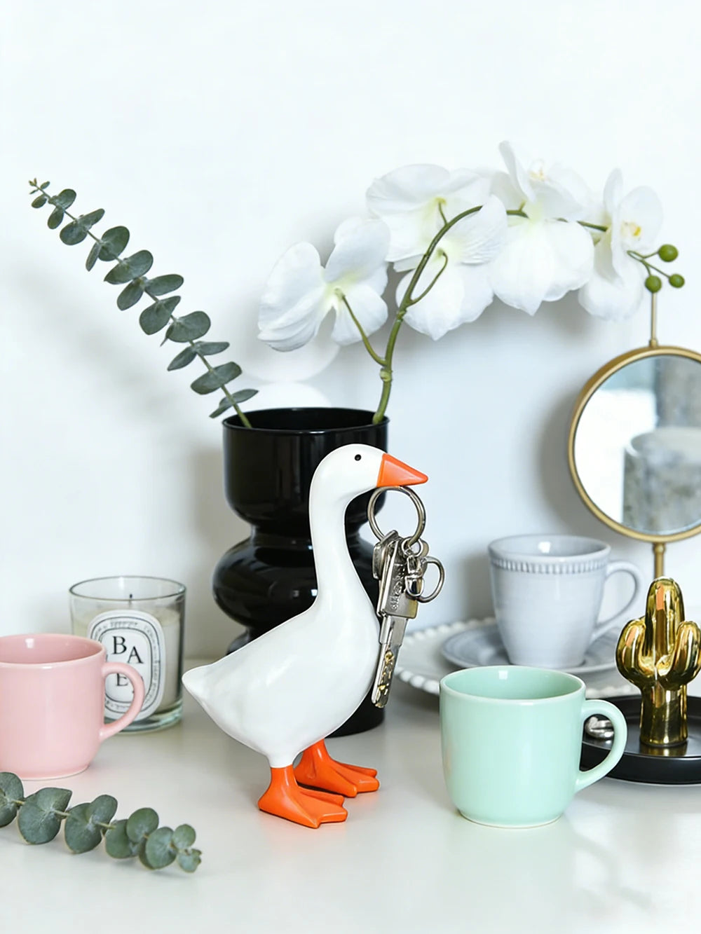 A white resin goose key holder sculpture next to a potted orchid and green eucalyptus leaves.