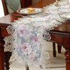 A lace table runner featuring a floral pattern in pink and gray on a dark wood table.
