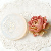 Un moule en silicone en forme de rose rose pour cire de bougie repose sur un chemin de table en dentelle blanche.