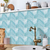 A bathroom featuring light blue herringbone marble peel-and-stick tiles on the wall and a brass faucet.
