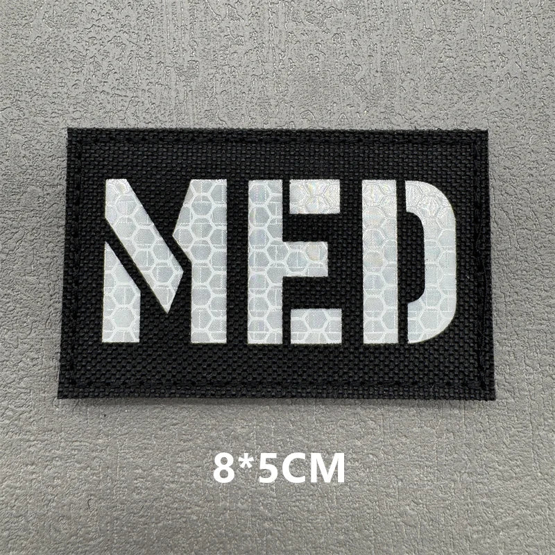 Black woven patch with white letters MED on a gray background