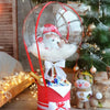 A clear balloon filled with a Santa face is tied to a red container next to a decorated Christmas tree.