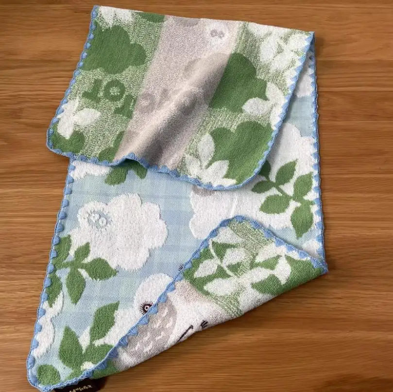 A folded pure cotton embroidered cartoon face towel featuring green and white floral patterns.
