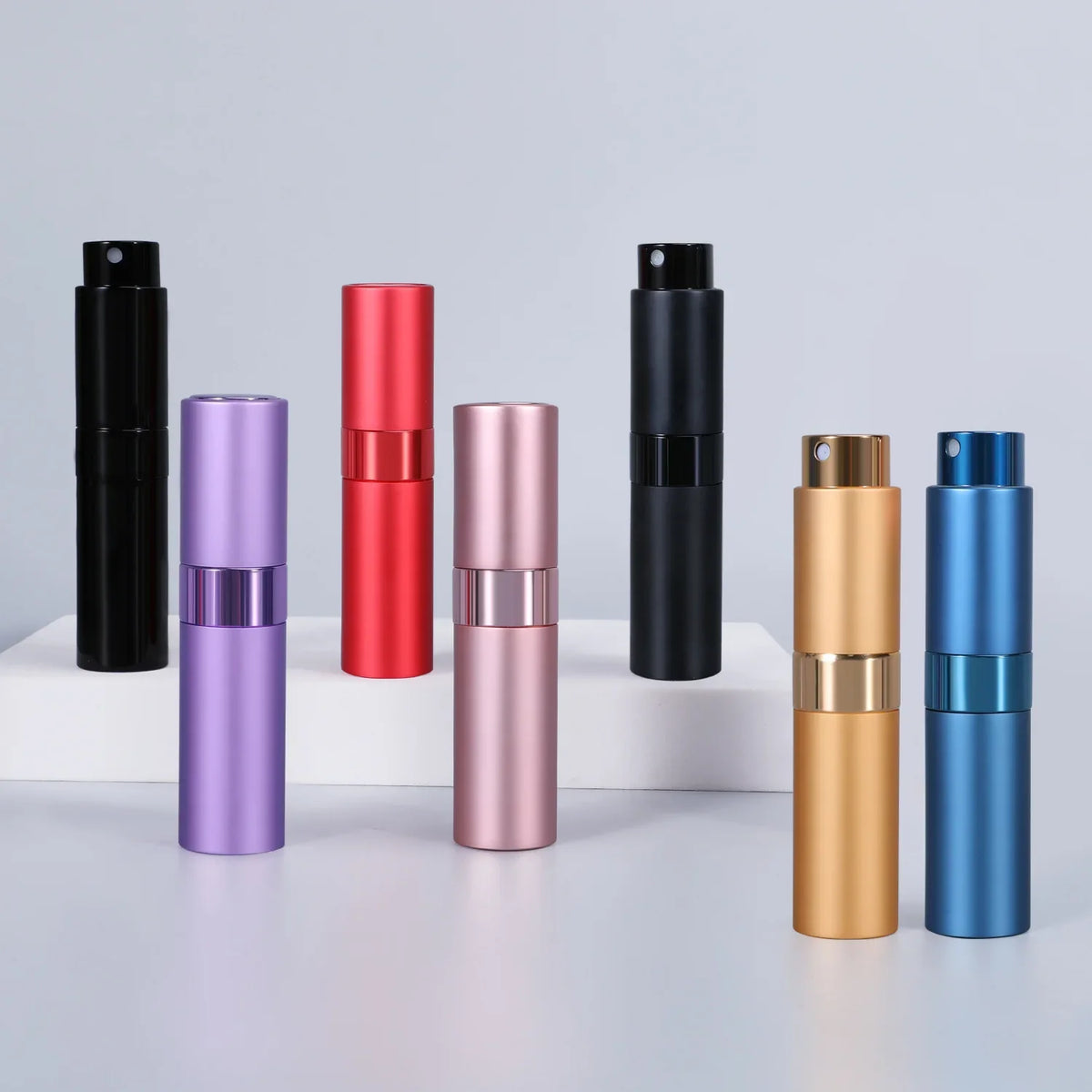 A collection of refillable aluminum perfume atomizers in black, red, purple, rose gold, and blue, displayed on a white surfac