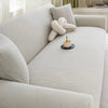 A light beige stretch jacquard sofa cover with a textured weave and a decorative knitted pillow on a sofa.