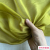 A hand is folding a piece of bright yellow silk chiffon fabric.