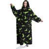 A woman wearing an oversized black hoodie blanket featuring a pattern of green dinosaurs and tropical leaves.