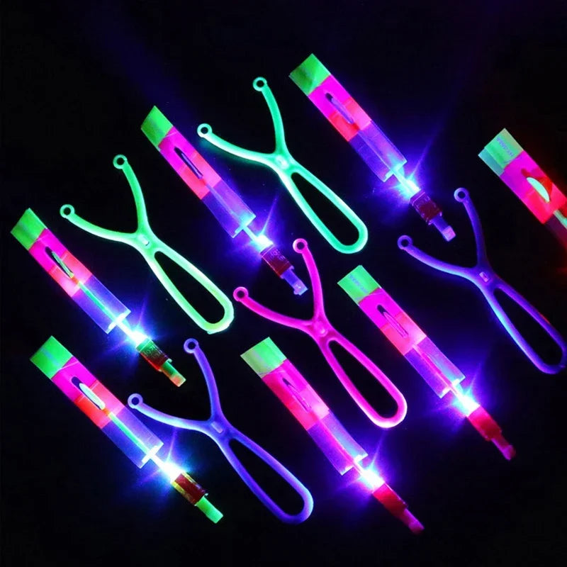 A collection of LED glowing flying arrow toys with rubber band launchers in various bright colors against a dark background.