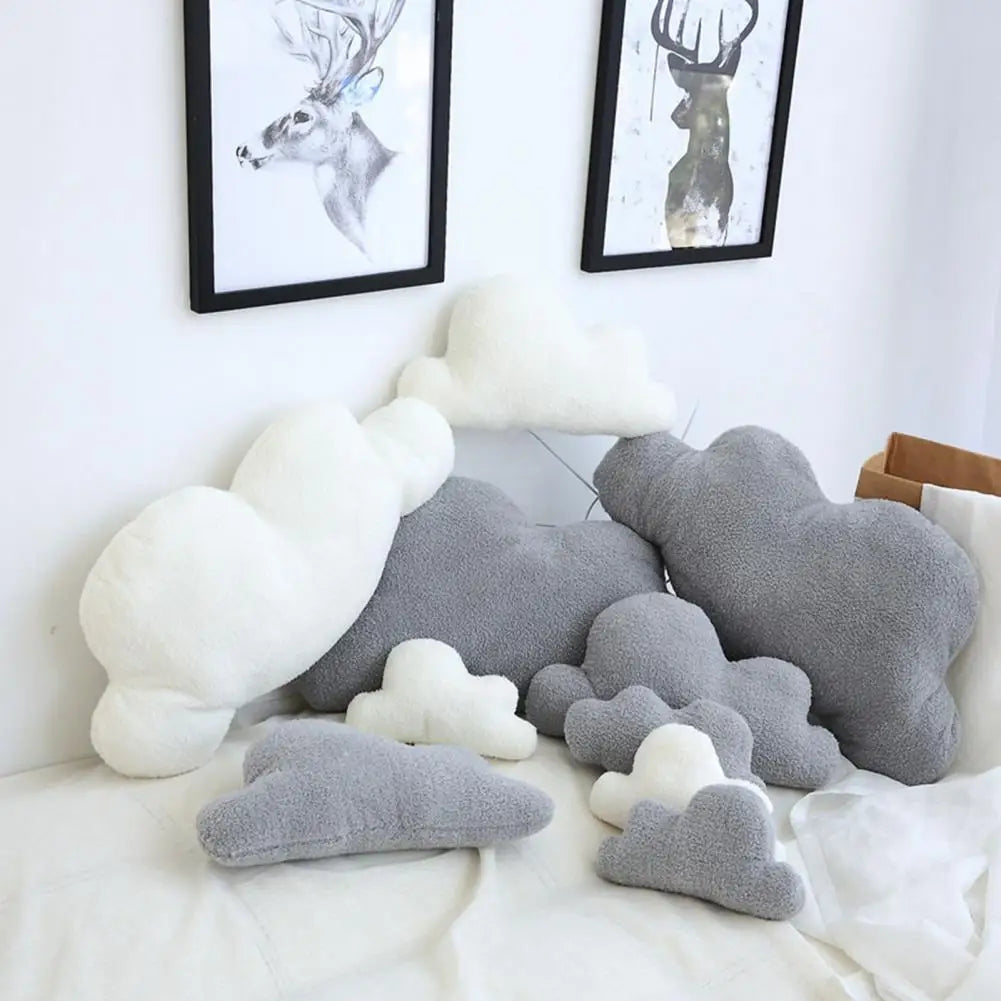 A collection of cloud-shaped plush throw pillows in white and gray resting on a white bed.