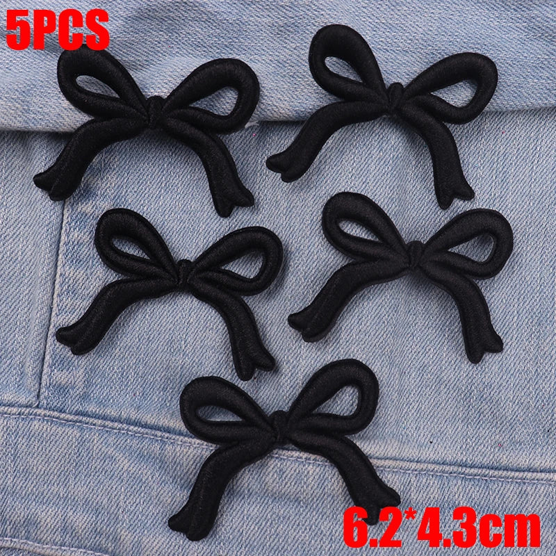 Five black fabric bows are displayed on a denim fabric surface.