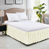 A white bed with a ruffled cream-colored elastic wrap-around skirt and white pillows in a bedroom setting.