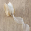 A roll of sheer, cream-colored organza ribbon with a wavy edge lying on a wooden surface.
