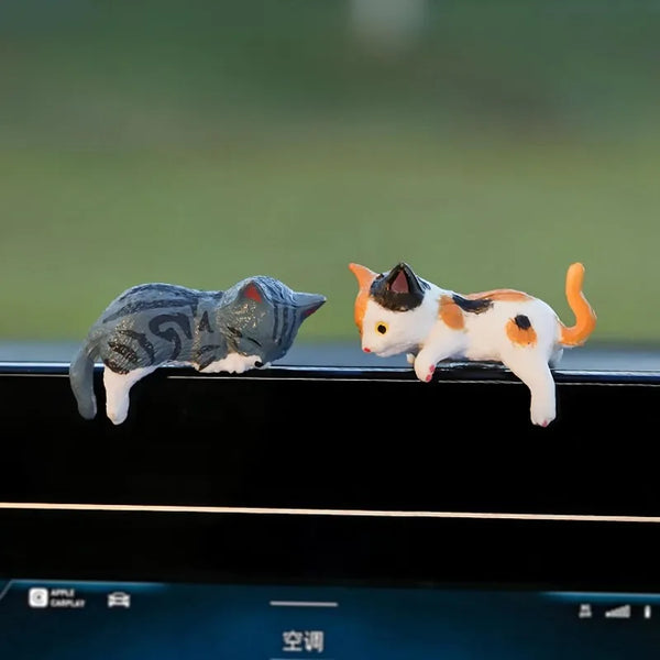 A white and gray cartoon cat ornament is placed on a black car dashboard.