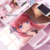 A close-up of a pink-haired anime girl character displayed on a mouse pad or desk mat with various accessories.