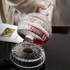 A hand is pouring a reddish-pink liquid from a handcrafted crystal wine decanter with a rotating aerator.