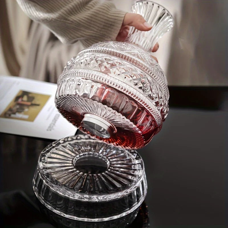 A hand is pouring a reddish-pink liquid from a handcrafted crystal wine decanter with a rotating aerator.