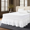 Un lit blanc avec jupon élastique anti-poussière et des oreillers blancs dans une chambre moderne.
