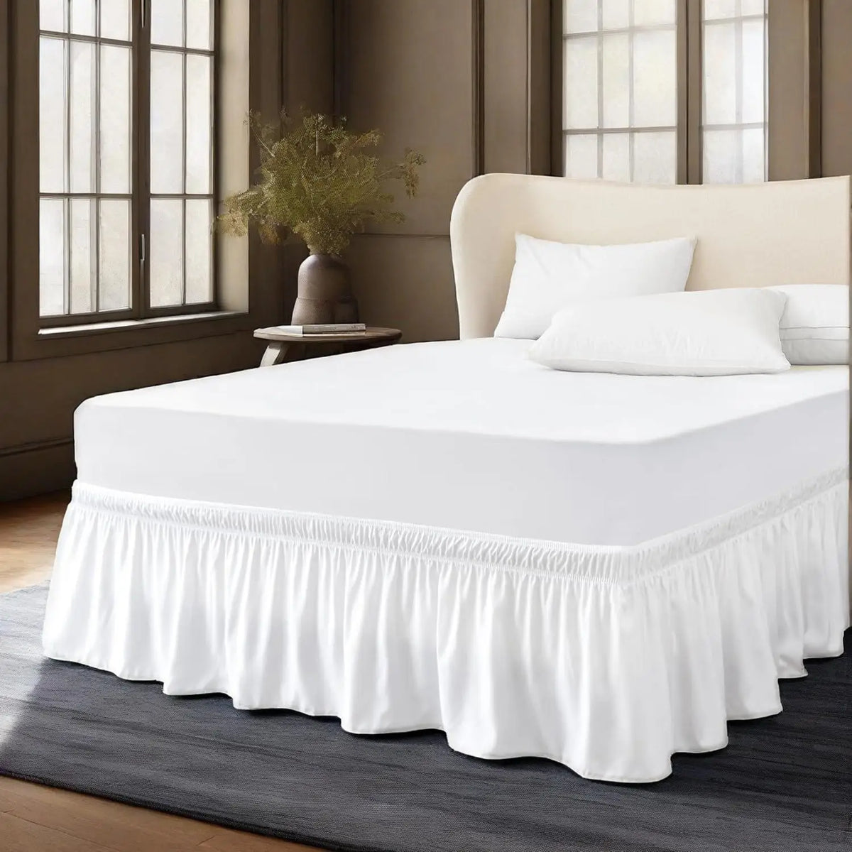Un lit blanc avec jupon élastique anti-poussière et des oreillers blancs dans une chambre moderne.