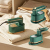A teal handheld garment steamer is shown resting on a beige linen cloth next to wooden tools.