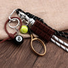 A metal 8-ball keychain featuring a sleek black finish, attached to a leather cord and a wooden golf-style racket.