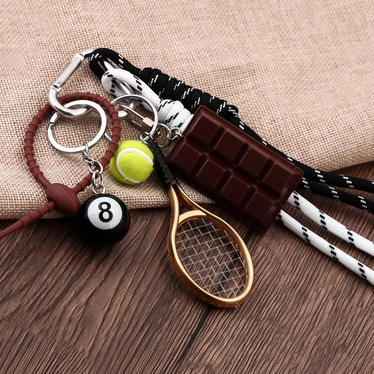 A metal 8-ball keychain featuring a sleek black finish, attached to a leather cord and a wooden golf-style racket.