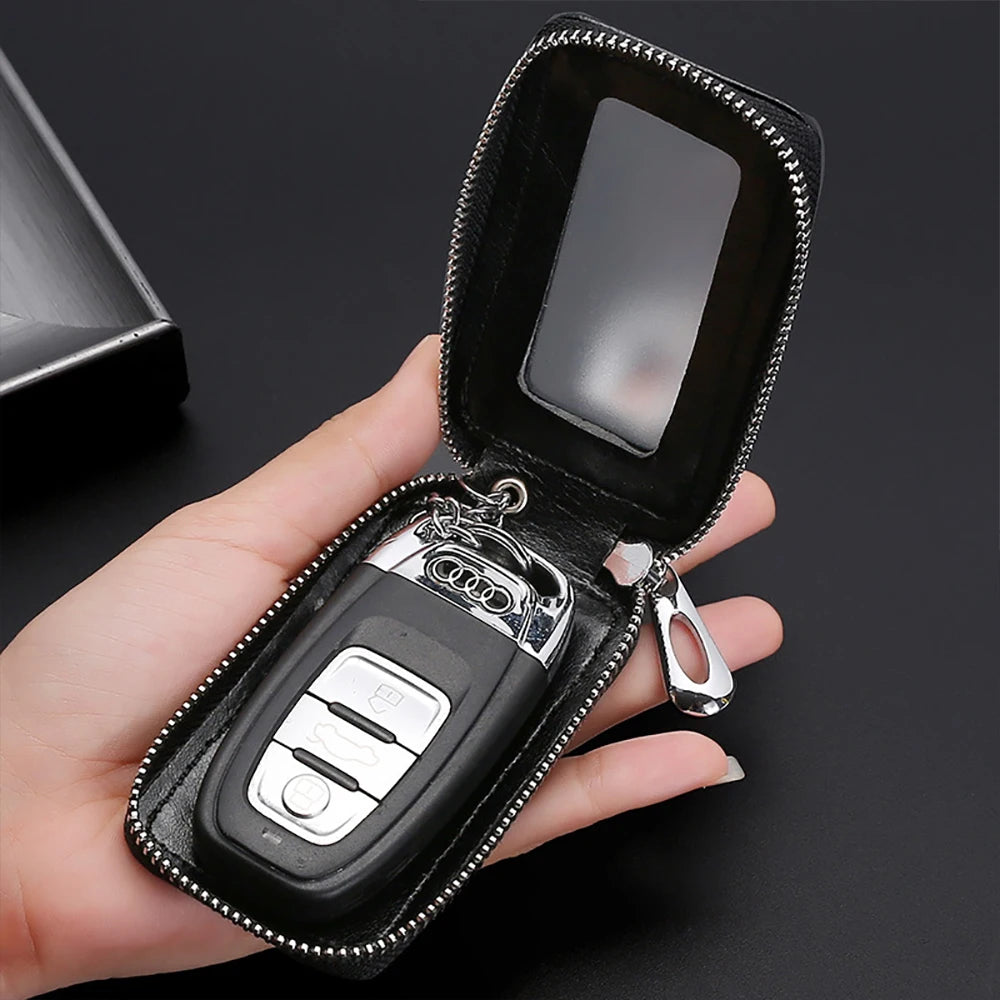 A hand holds an open black leather key holder with a transparent window pocket and a silver keychain.