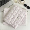 A quilted pink laptop sleeve with a zipper is placed next to a silver perfume bottle and a white cup on a light surface.