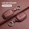 A brown genuine leather car key holder with a metal ring, shown on a dark pink background.