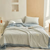 A light blue and white striped breathable summer quilt is displayed on a bed with a wooden headboard.