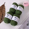 A pile of dark green Milk Cotton yarn balls with white labels on a white surface.