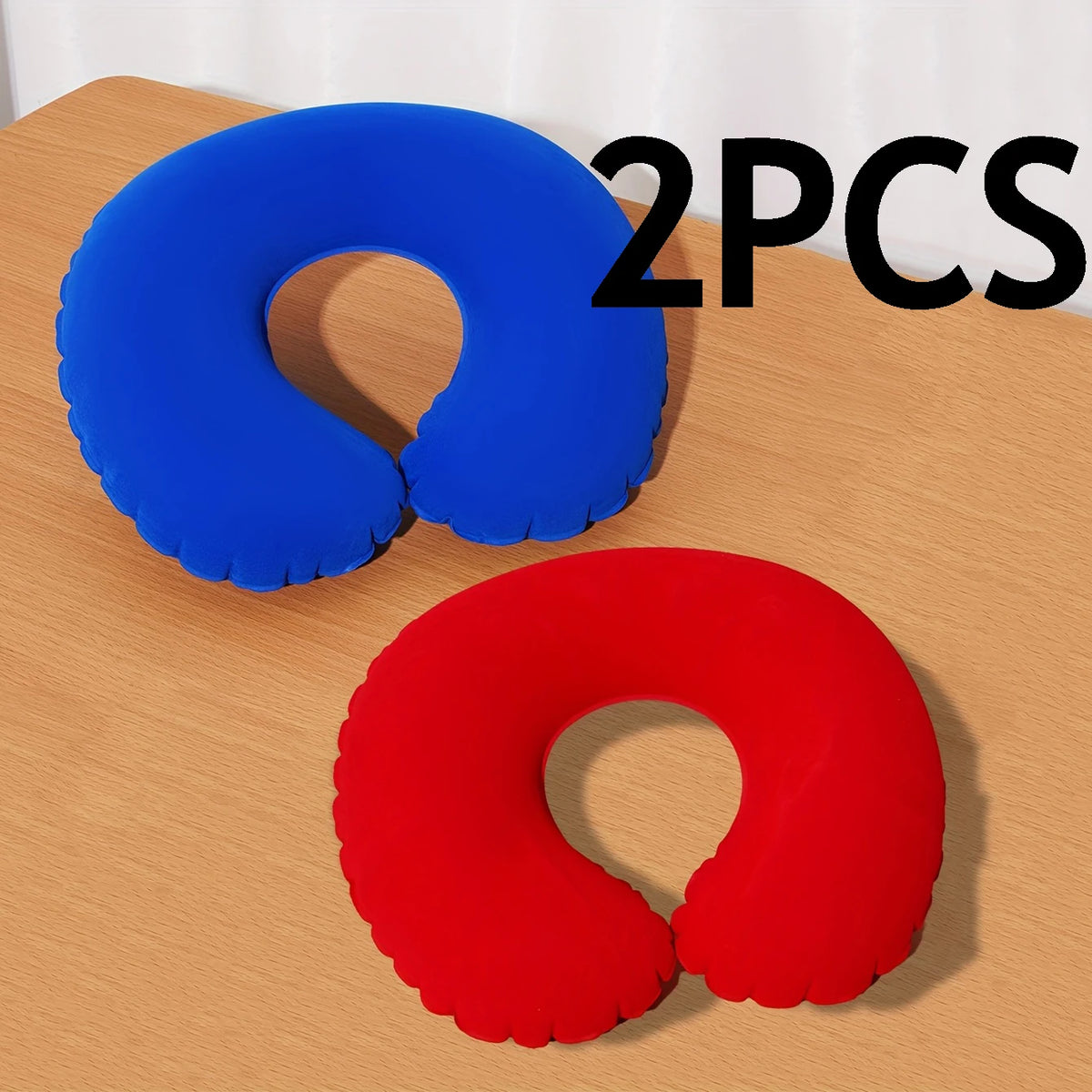 Two inflatable U-shaped travel neck pillows, one blue and one red, displayed on a wooden surface.