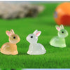A set of three cute resin miniature bunny figurines in shades of yellow, white, and light green resting on green grass.