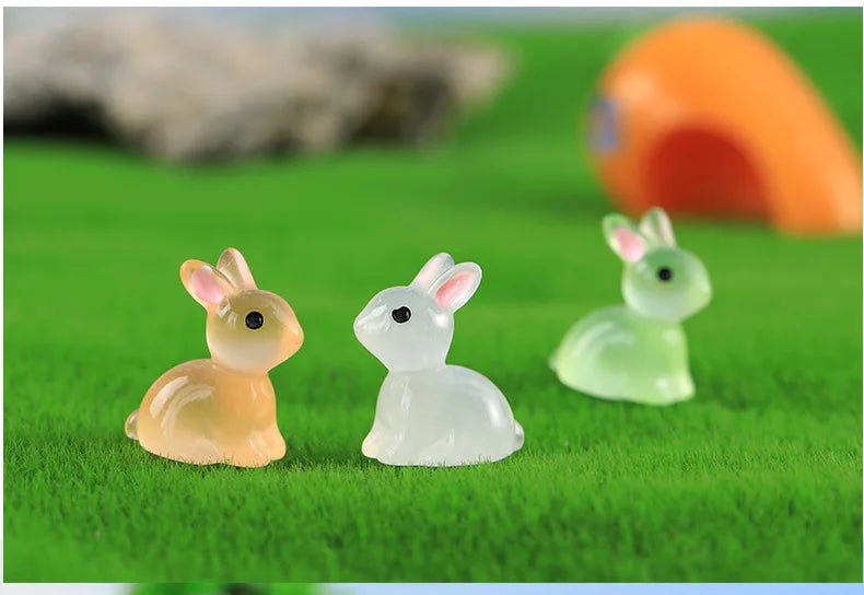 A set of three cute resin miniature bunny figurines in shades of yellow, white, and light green resting on green grass.