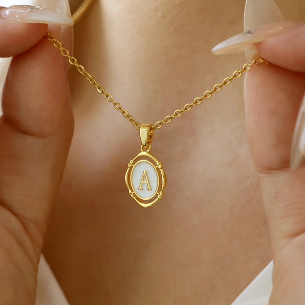 Eine goldene Halskette mit einem A-förmigen Anhänger wird von den Fingern einer Person gehalten.