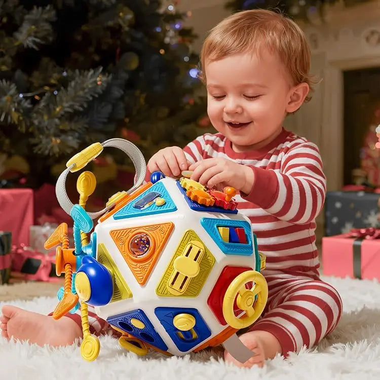 A smiling toddler is playing with a colorful 22-in-1 busy board activity cube on a white rug.