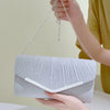A hand holds a silver pleated glitter envelope clutch with a detachable chain strap against a light background.
