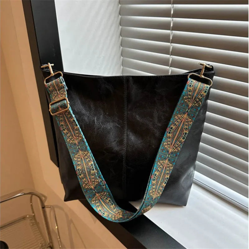 A black vintage bohemian shoulder bag with golden embroidery hanging against a window blind.