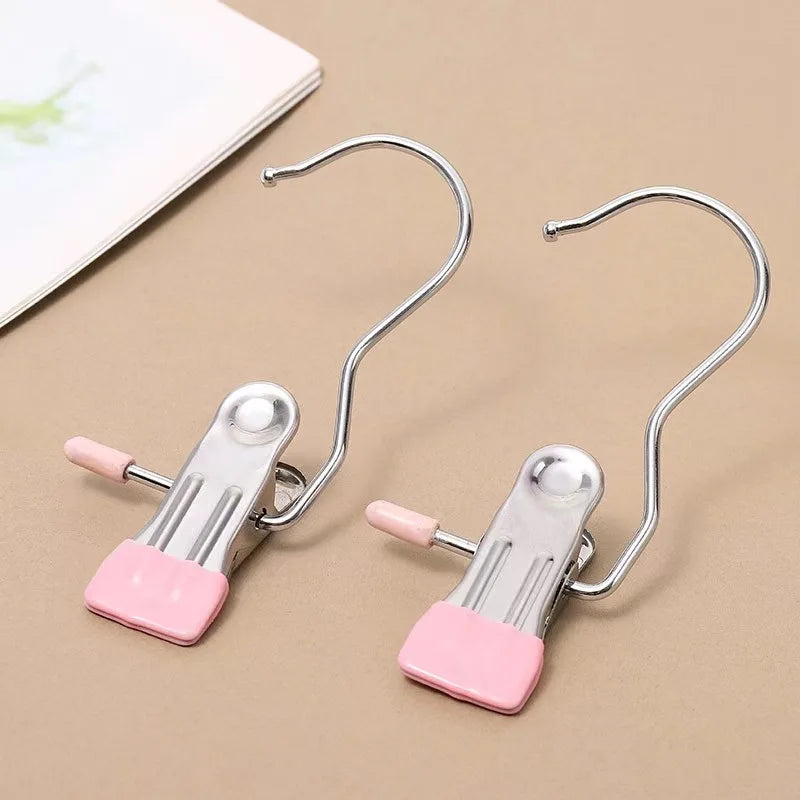 Two stainless steel clothespins with hooks and pink plastic grips are shown on a beige surface.