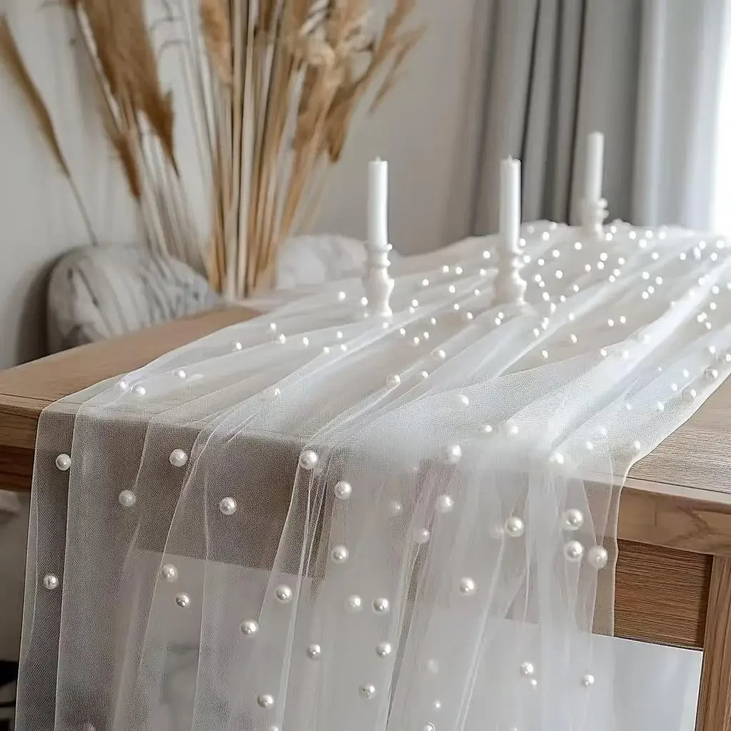 Elegant faux pearl tulle table runner draped over a wooden table with tall dried grasses and candles.