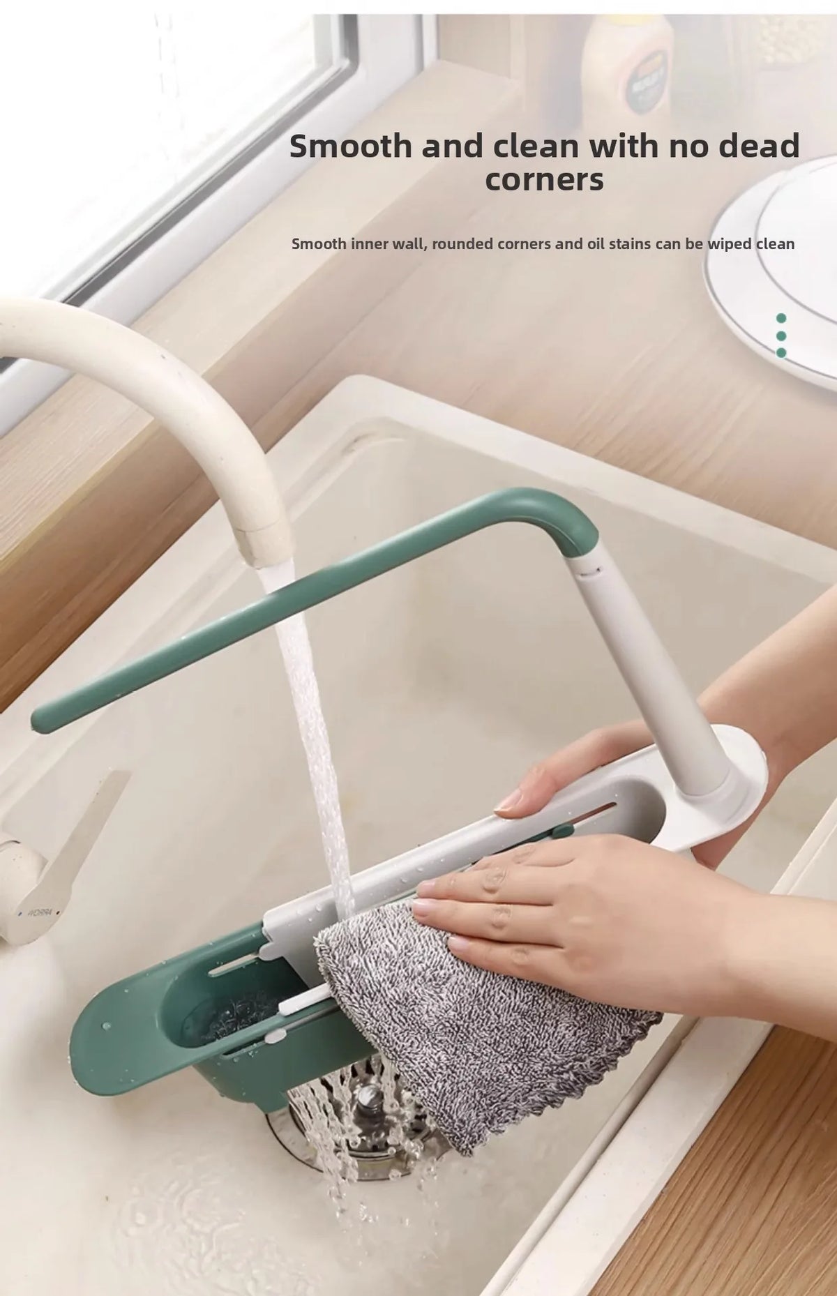 A hand is using an adjustable over-sink dish drying rack to clean a sink, demonstrating smooth inner corners and no dead corn