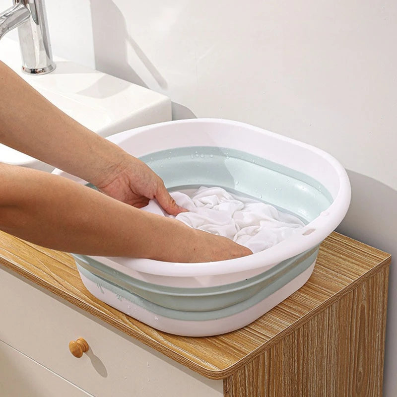 A hand is placing white cloth into a collapsible silicone washbasin on a wooden countertop.