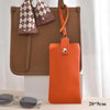An orange PU leather glasses case hanging from a brown tote bag with a checkered fabric detail.