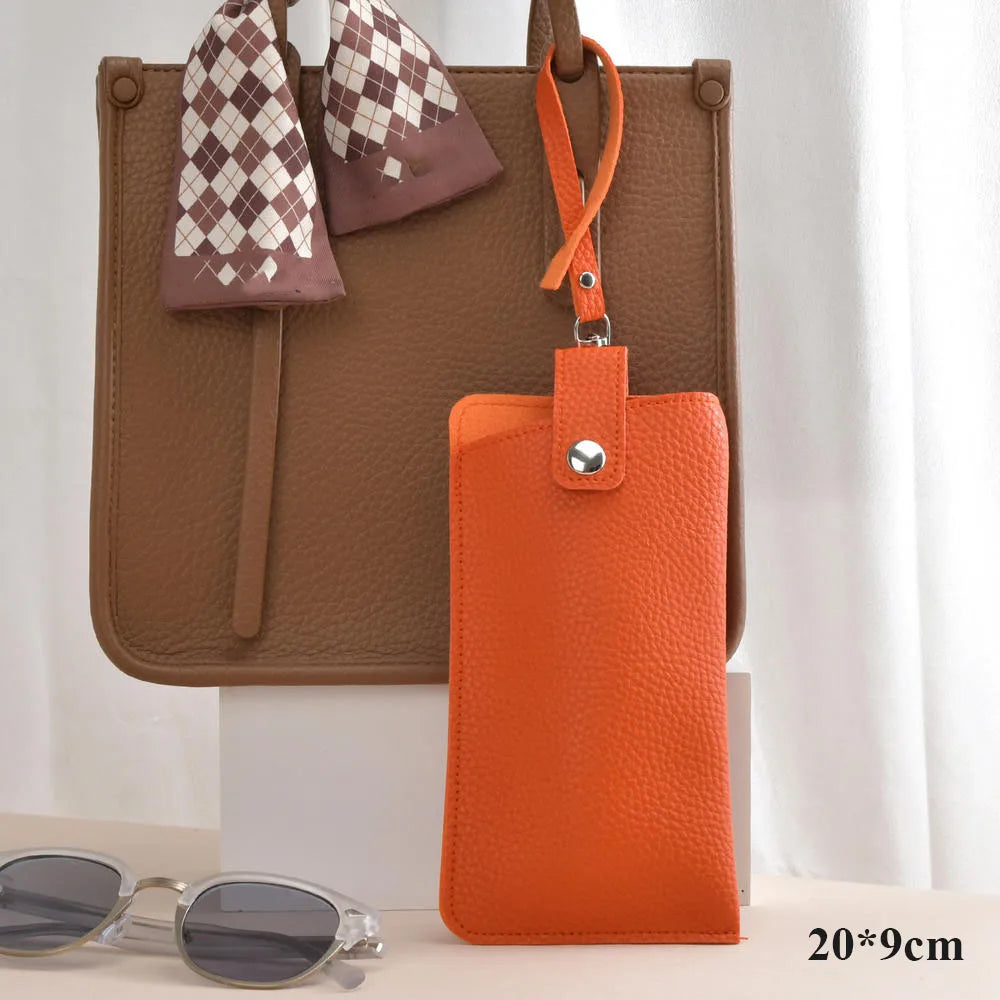 An orange PU leather glasses case hanging from a brown tote bag with a checkered fabric detail.